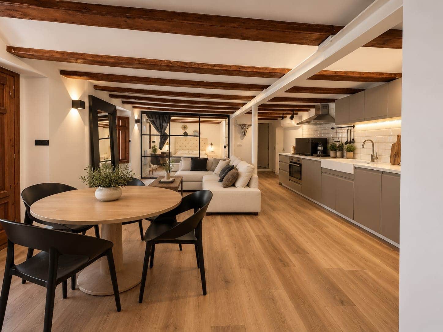 Salón y cocina abiertos con vigas de madera vistas y suelo vinílico de lama en roble claro